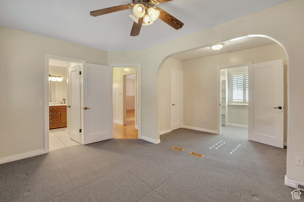 Unfurnished bedroom featuring a ceiling fan, arched walkways, baseboards, carpet floors, and connected bathroom