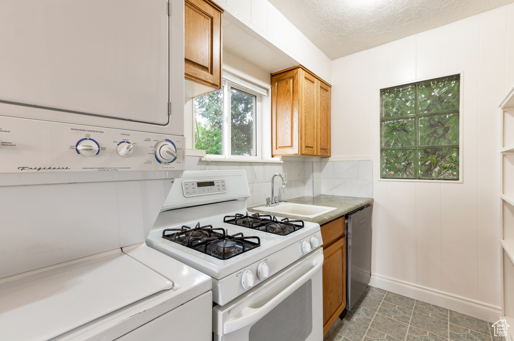 Kitchen with stacked washing maching and dryer, white gas range, light countertops, a sink, and dishwasher