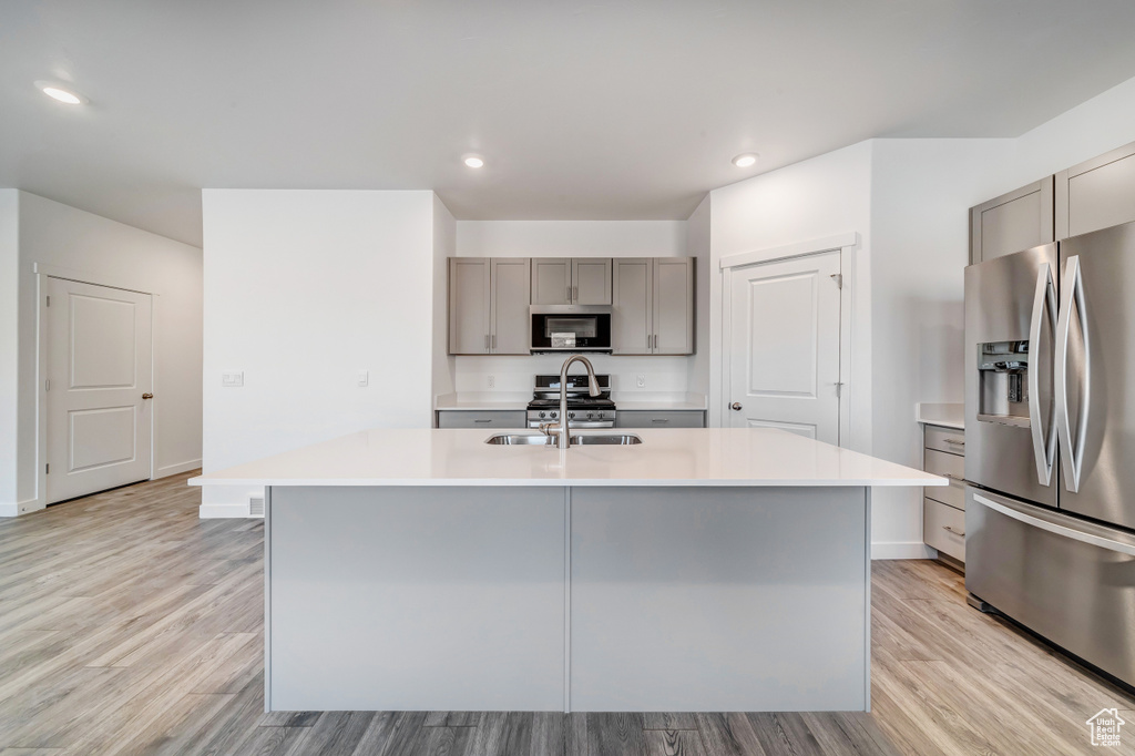 Kitchen with light countertops, gray cabinets, a sink, light wood-style flooring, and stainless steel appliances