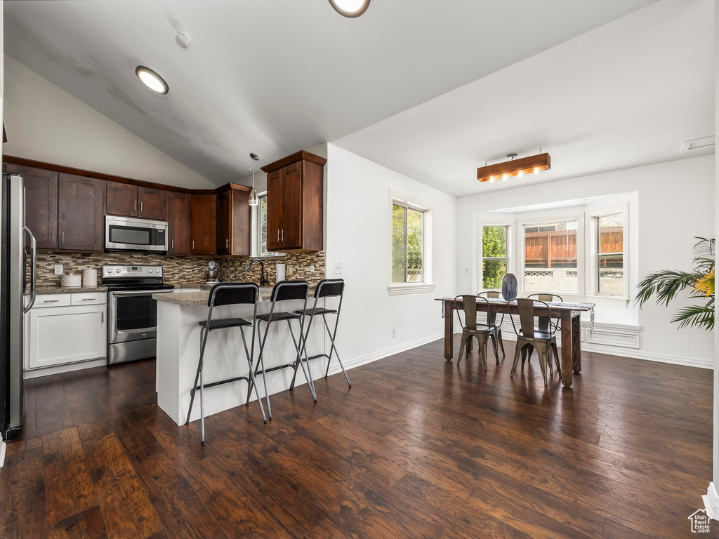 Kitchen featuring a peninsula, a breakfast bar, dark wood-style floors, backsplash, and stainless steel appliances