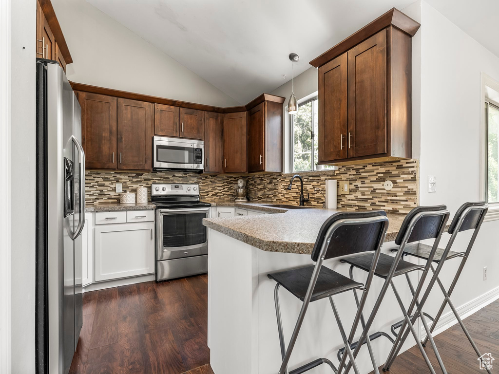 Kitchen featuring appliances with stainless steel finishes, vaulted ceiling, a sink, a peninsula, and dark wood-type flooring