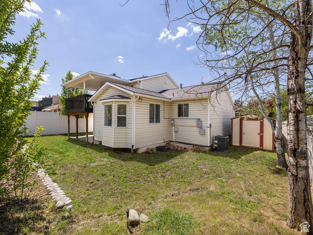 Rear view of house featuring an outdoor structure, fence, a balcony, a storage unit, and a lawn