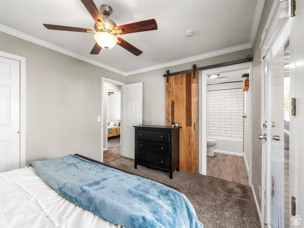 Carpeted bedroom featuring crown molding, baseboards, a barn door, connected bathroom, and a ceiling fan