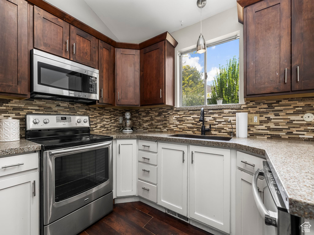 Kitchen with backsplash, appliances with stainless steel finishes, a sink, and dark wood-type flooring