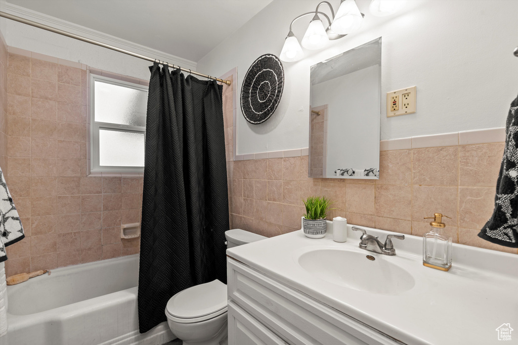 Full bath with vanity, wainscoting, shower / bath combination with curtain, toilet, and tile walls