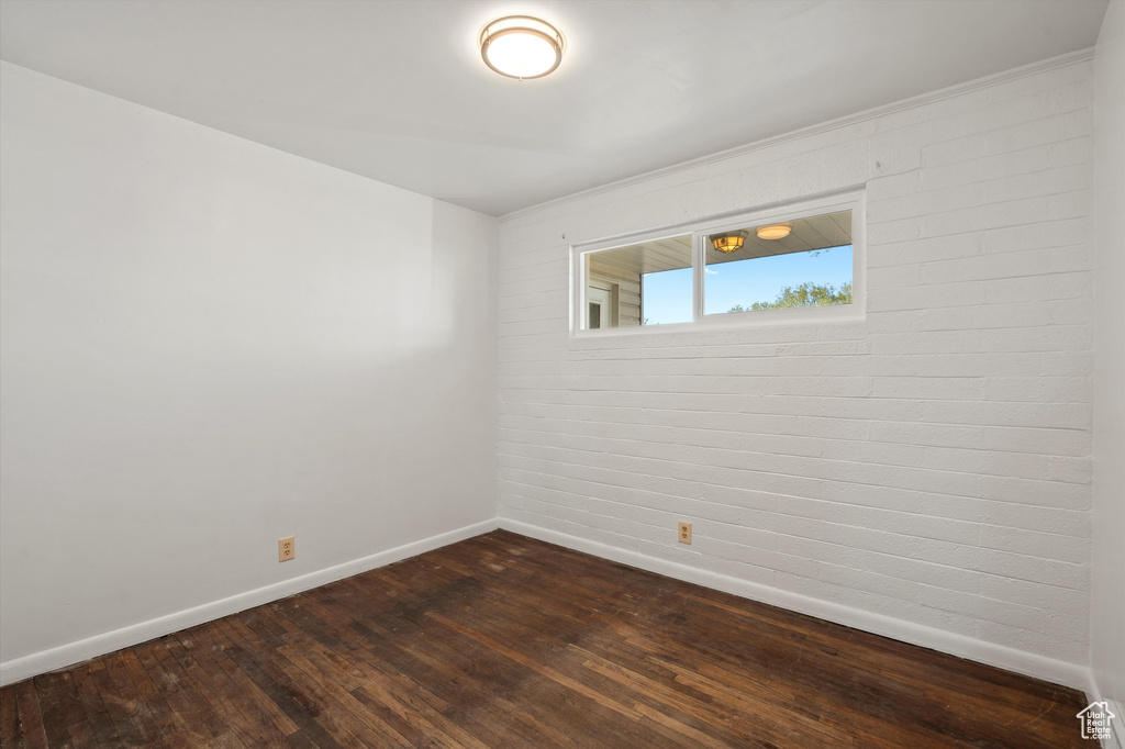 Unfurnished room with baseboards, dark wood-style floors, and brick wall