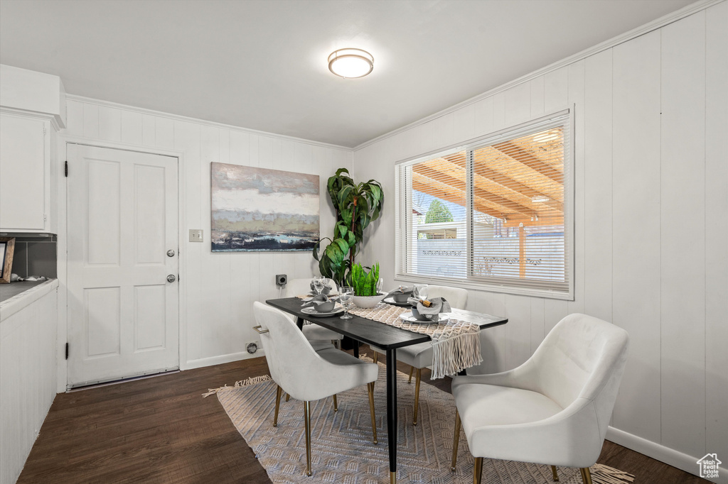 Dining room featuring crown molding, baseboards, dark wood-style floors, and a decorative wall