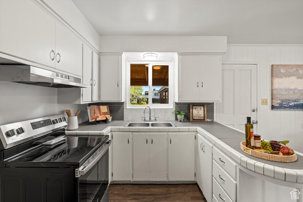 Kitchen featuring tile counters, under cabinet range hood, white cabinets, stainless steel electric stove, and a sink