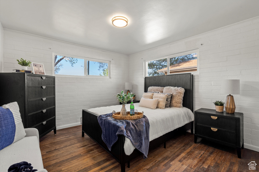 Bedroom featuring baseboards, dark wood-style flooring, and brick wall
