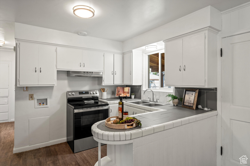 Kitchen featuring a sink, tile counters, white cabinetry, under cabinet range hood, and stainless steel electric stove