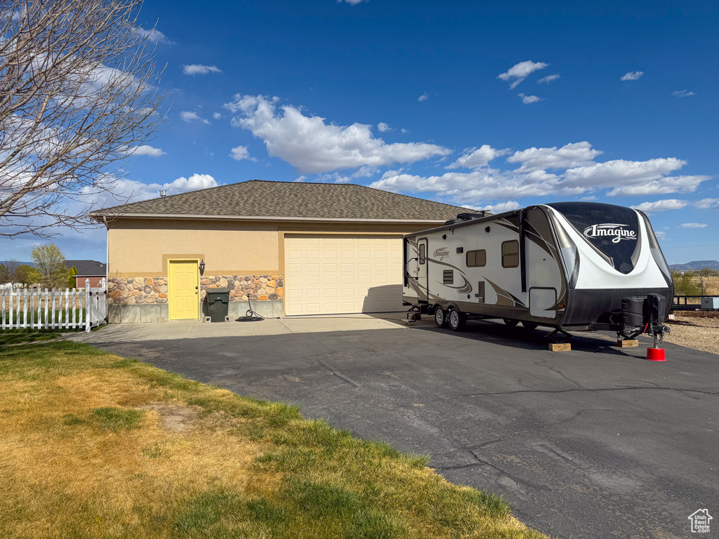 View of side of home with a garage, fence, stone siding, stucco siding, and driveway