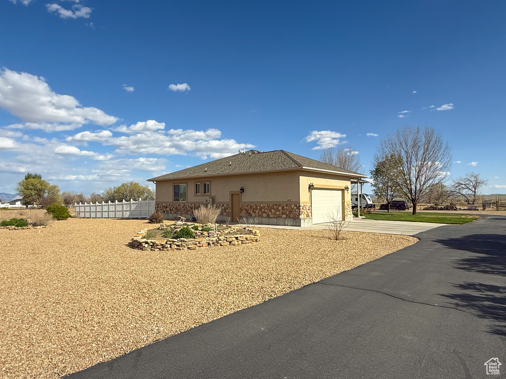 View of side of property featuring fence, stone siding, stucco siding, concrete driveway, and an attached garage