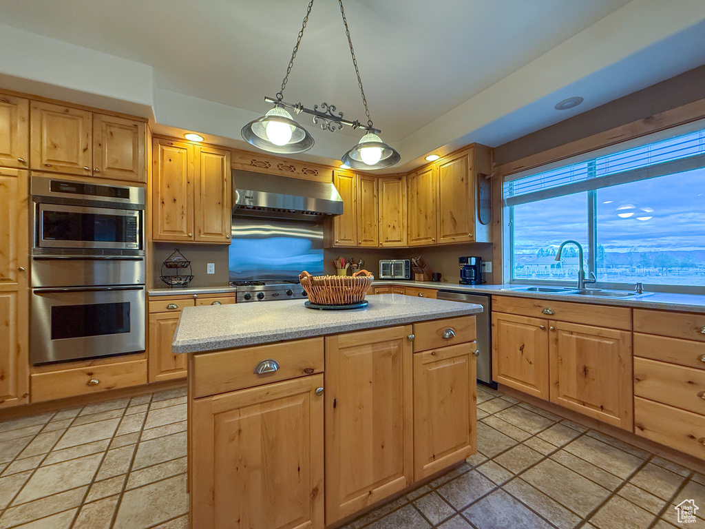 Kitchen with wall chimney range hood, appliances with stainless steel finishes, a sink, light brown cabinets, and stone tile floors