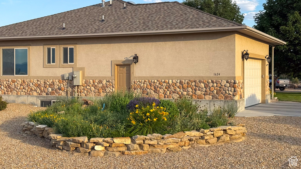 View of property exterior featuring stone siding, stucco siding, a shingled roof, and a garage