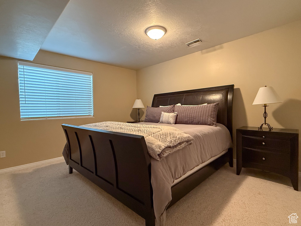 Bedroom featuring light colored carpet, a textured ceiling, visible vents, and baseboards
