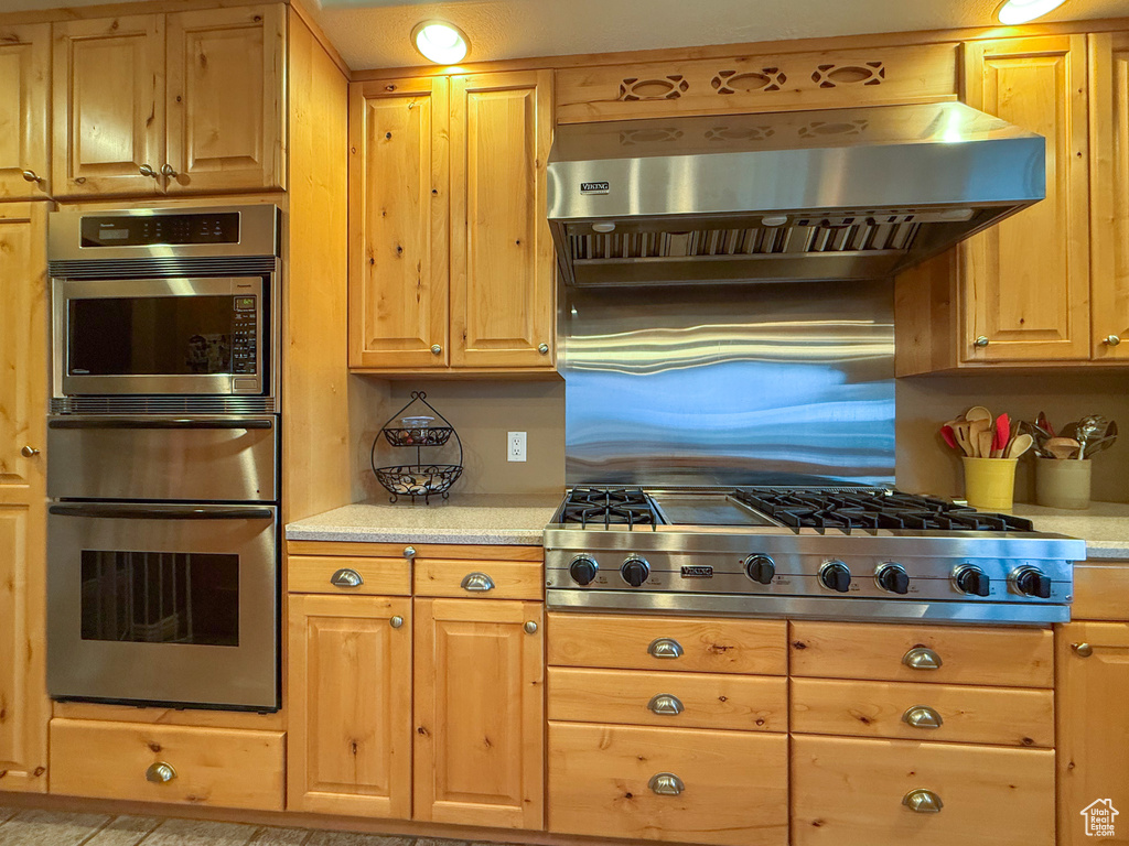 Kitchen with stainless steel gas cooktop, exhaust hood, built in microwave, and light countertops