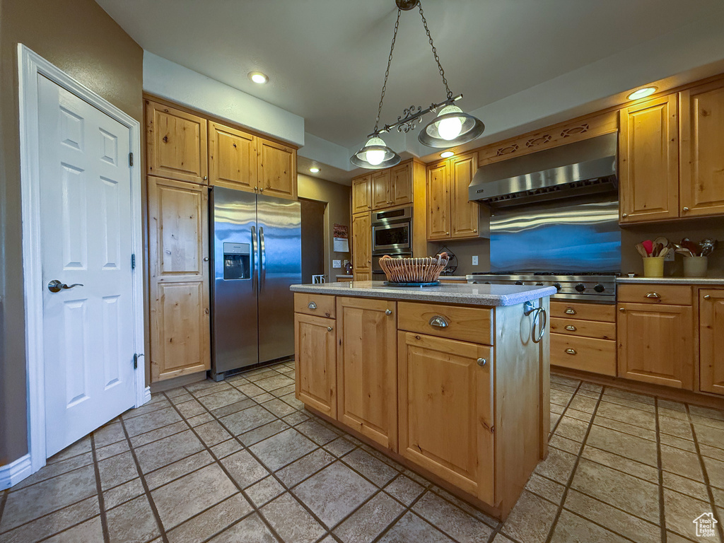 Kitchen with wall chimney range hood, light countertops, stone tile floors, stainless steel appliances, and a kitchen island