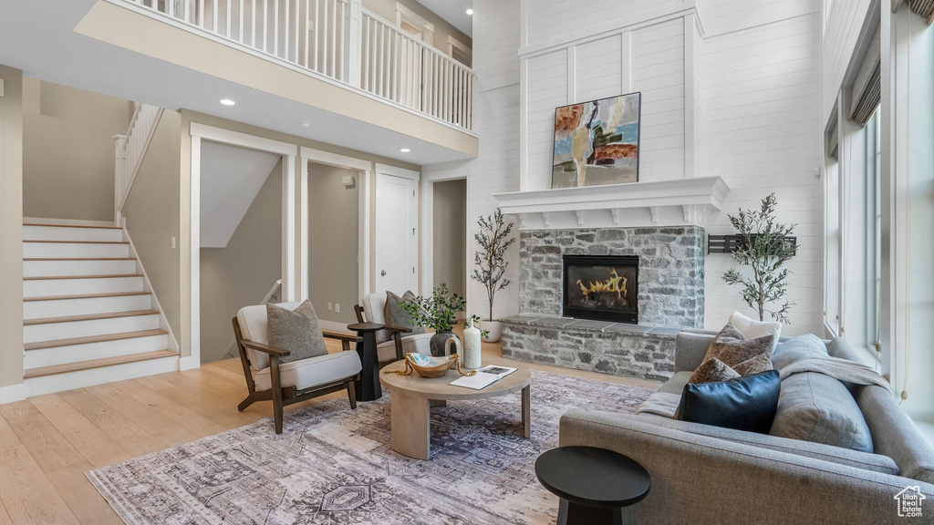 Living area with wood-type flooring, stairs, a towering ceiling, a stone fireplace, and recessed lighting