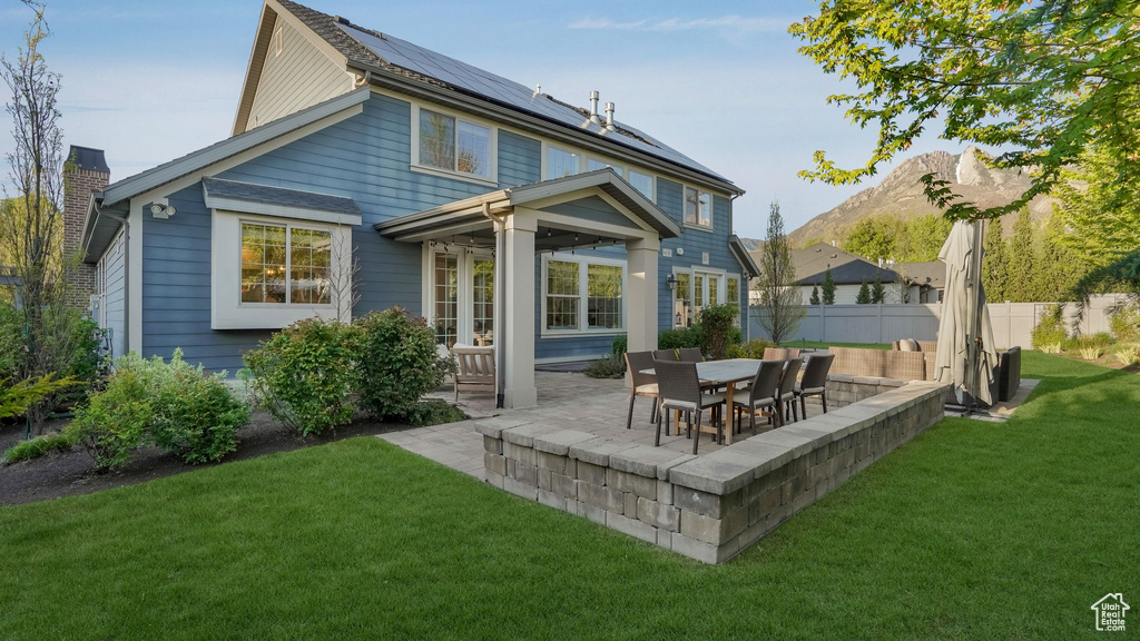 Back of property with roof mounted solar panels, fence, a lawn, and a patio area
