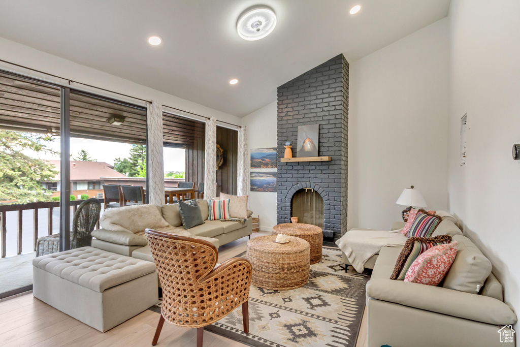 Living room featuring light wood-style floors, a fireplace, vaulted ceiling, and recessed lighting