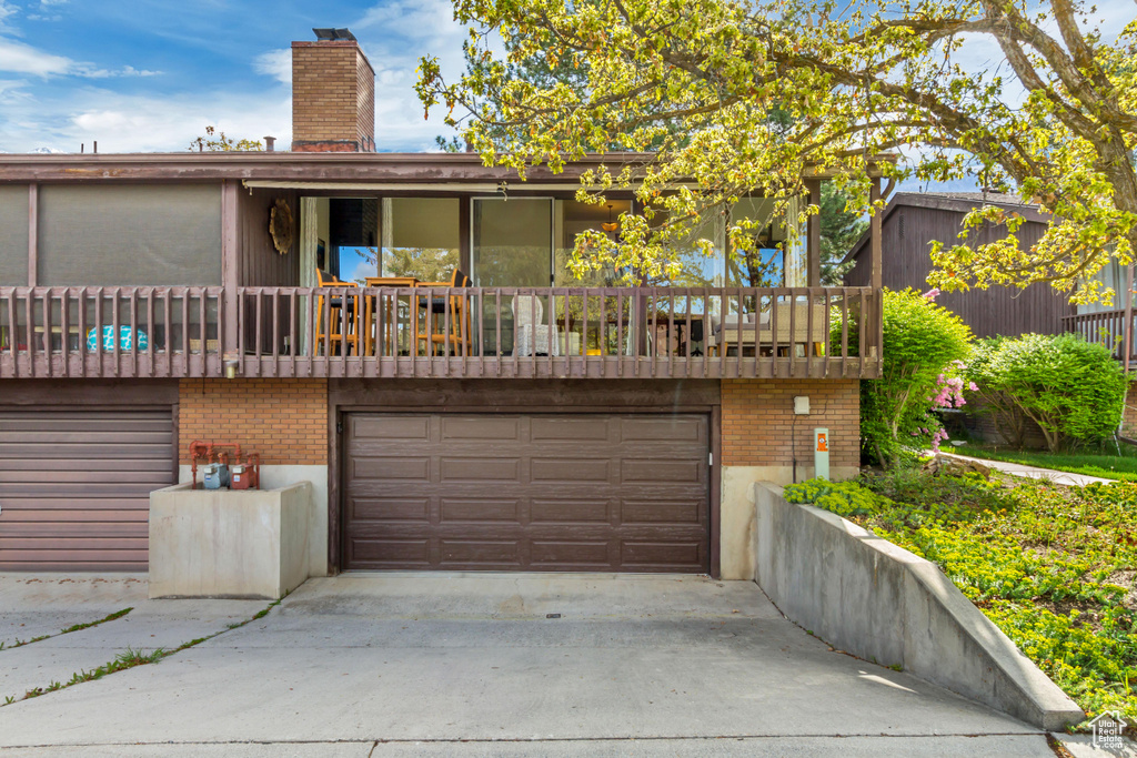 View of front of property featuring concrete driveway, brick siding, a chimney, and a garage