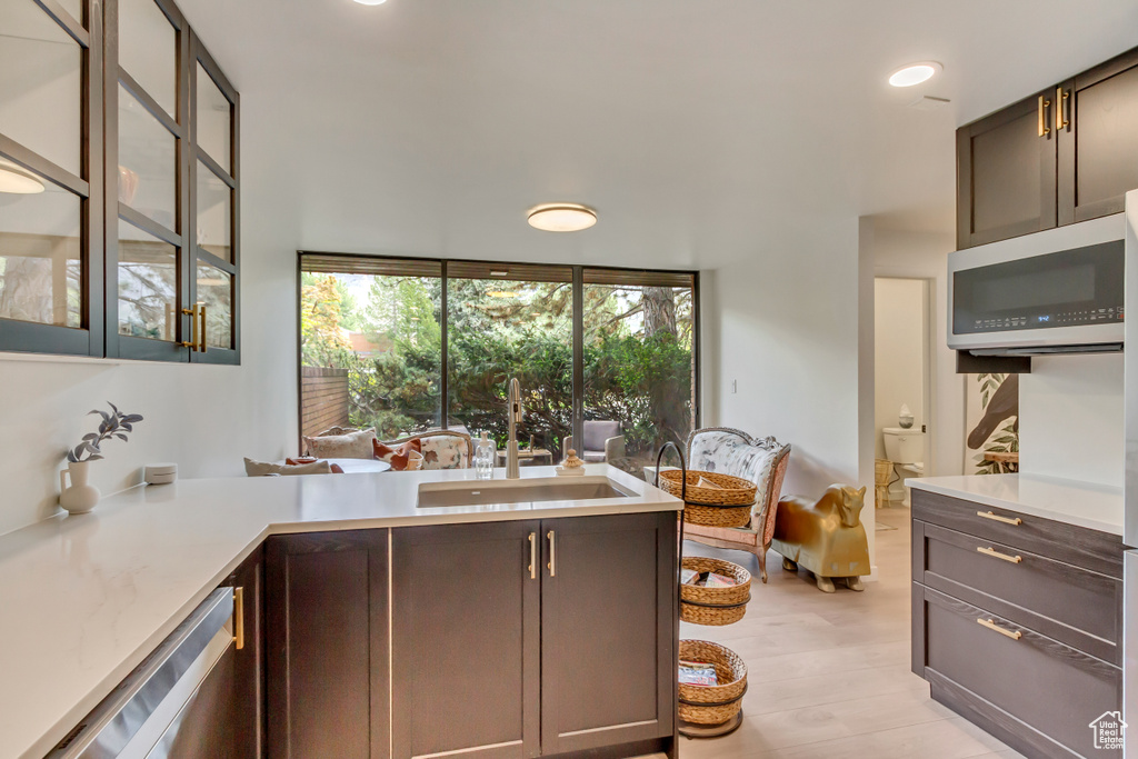 Kitchen with a sink, light countertops, stainless steel dishwasher, and glass insert cabinets