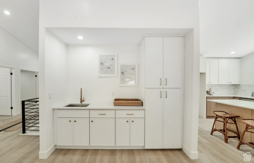 Kitchen with a sink, light wood finished floors, light countertops, recessed lighting, and white cabinetry