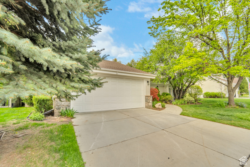 View of front of house featuring an attached garage, stone siding, stucco siding, a front yard, and concrete driveway
