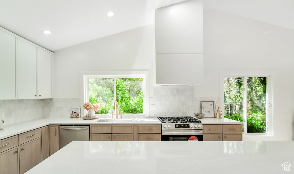 Kitchen with light stone counters, appliances with stainless steel finishes, a sink, lofted ceiling, and tasteful backsplash