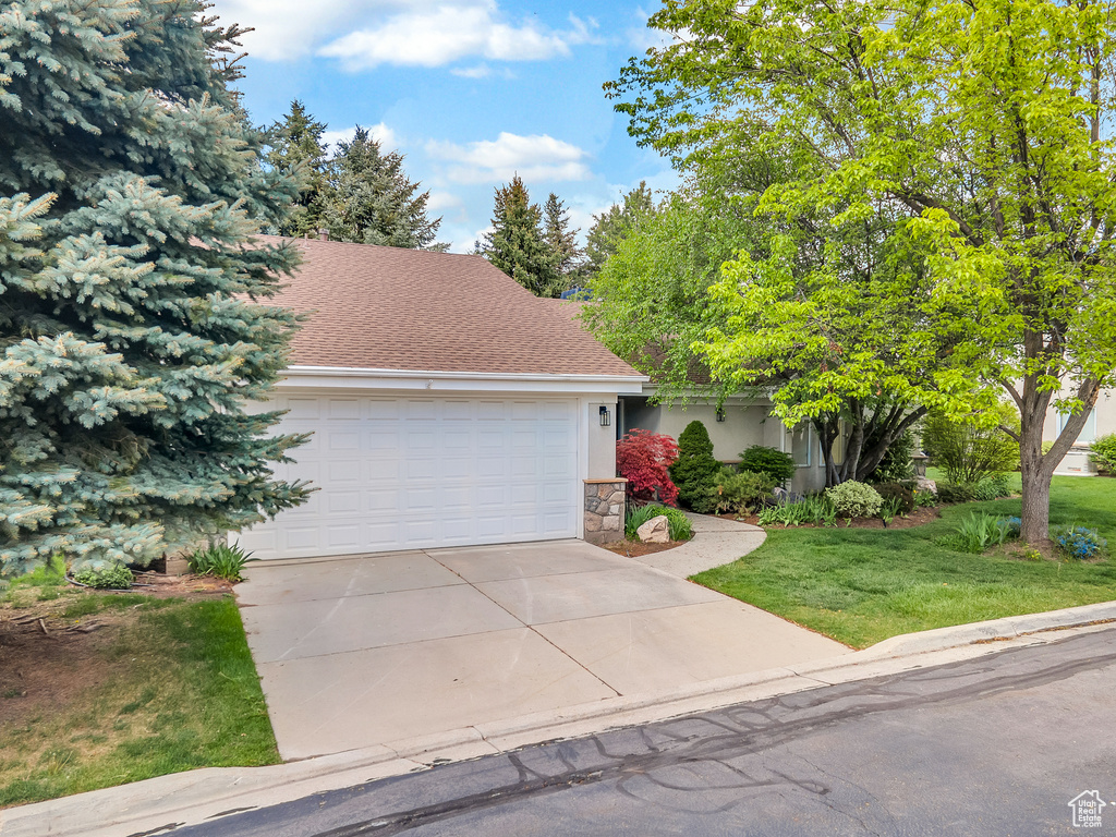 View of front of house featuring an attached garage, a shingled roof, a front lawn, stone siding, and concrete driveway