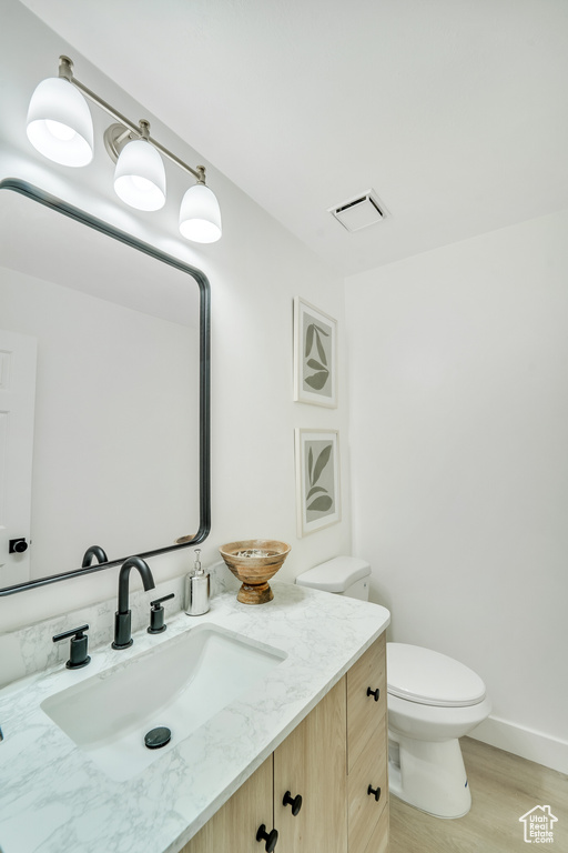 Half bathroom featuring vanity, toilet, baseboards, wood finished floors, and visible vents