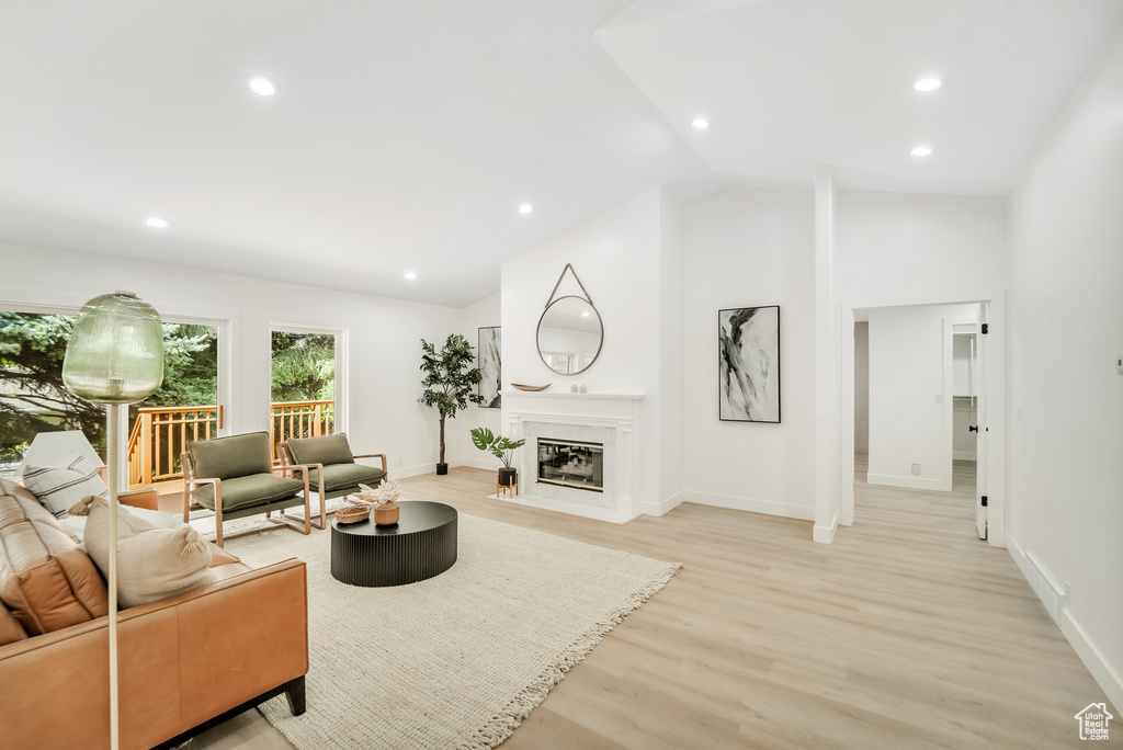 Living area with light wood-style flooring, recessed lighting, baseboards, a fireplace with flush hearth, and lofted ceiling