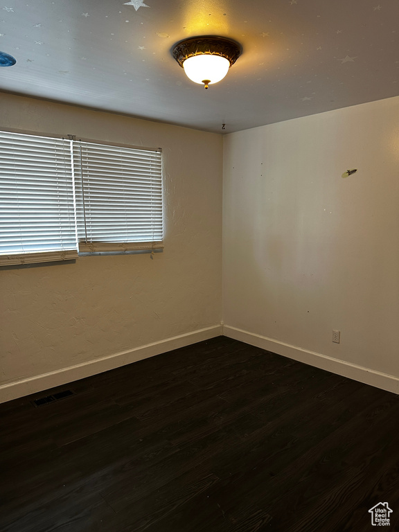 Empty room featuring dark wood-type flooring, baseboards, and visible vents