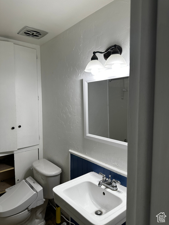 Bathroom with toilet, a textured wall, visible vents, and a sink