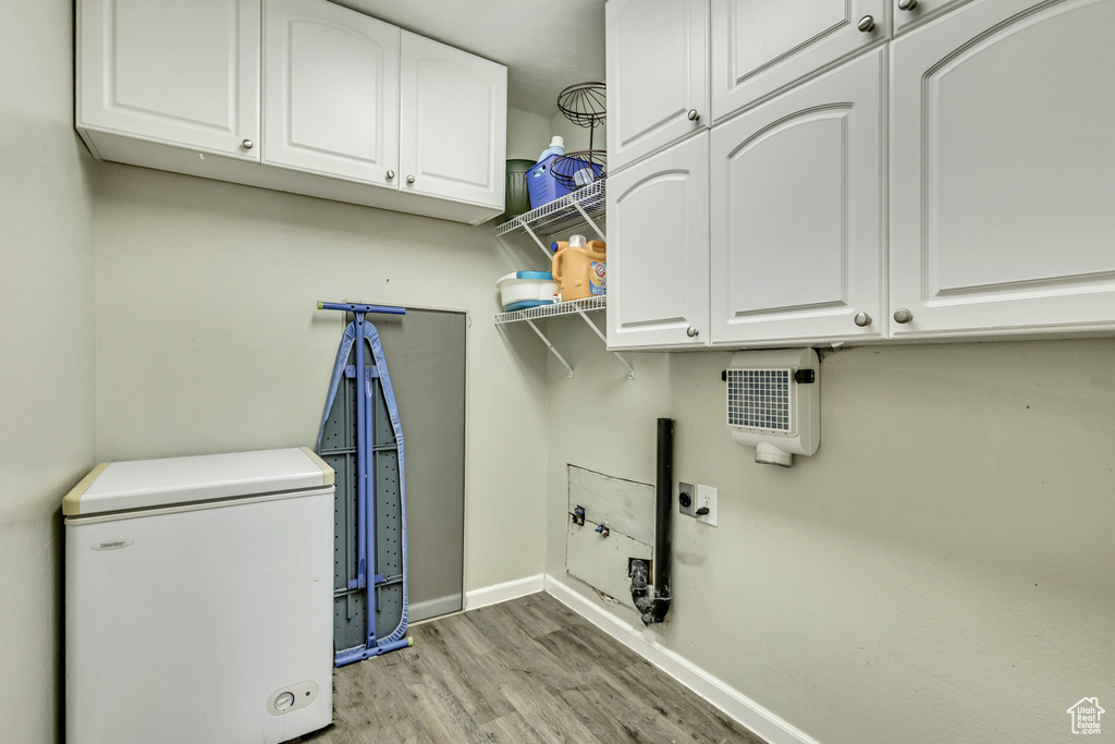 Clothes washing area featuring light wood-type flooring, cabinet space, baseboards, and hookup for an electric dryer