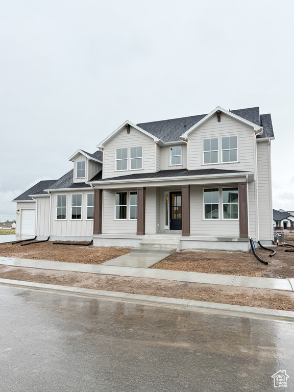 View of front facade featuring an attached garage, driveway, covered porch, and roof with shingles