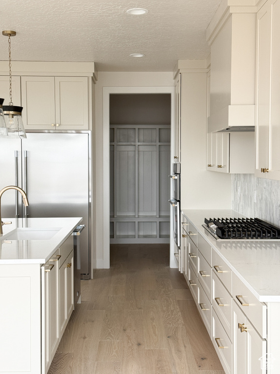 Kitchen featuring white cabinets, light countertops, wall chimney range hood, light wood-style floors, and appliances with stainless steel finishes