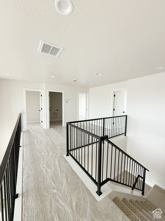 Corridor with a textured ceiling, visible vents, light colored carpet, and an upstairs landing