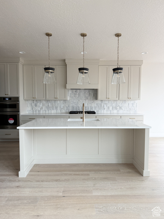 Kitchen featuring light countertops, a textured ceiling, multiple ovens, and decorative backsplash