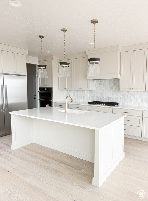 Kitchen featuring light countertops, a sink, gas cooktop, built in refrigerator, and decorative backsplash