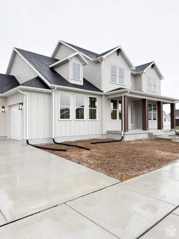 View of front of home featuring roof with shingles, driveway, covered porch, a garage, and board and batten siding