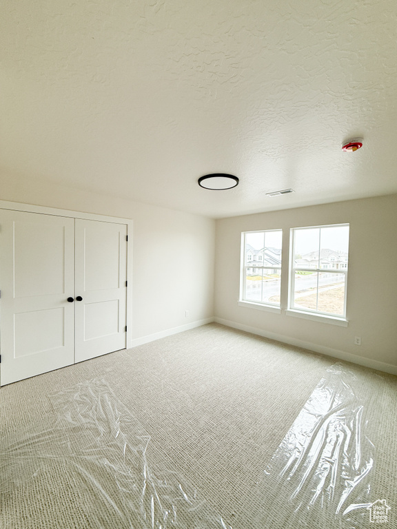 Empty room featuring light carpet, baseboards, visible vents, and a textured ceiling