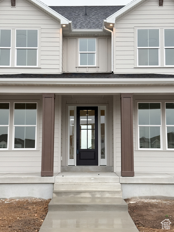 View of exterior entry with a porch and a shingled roof