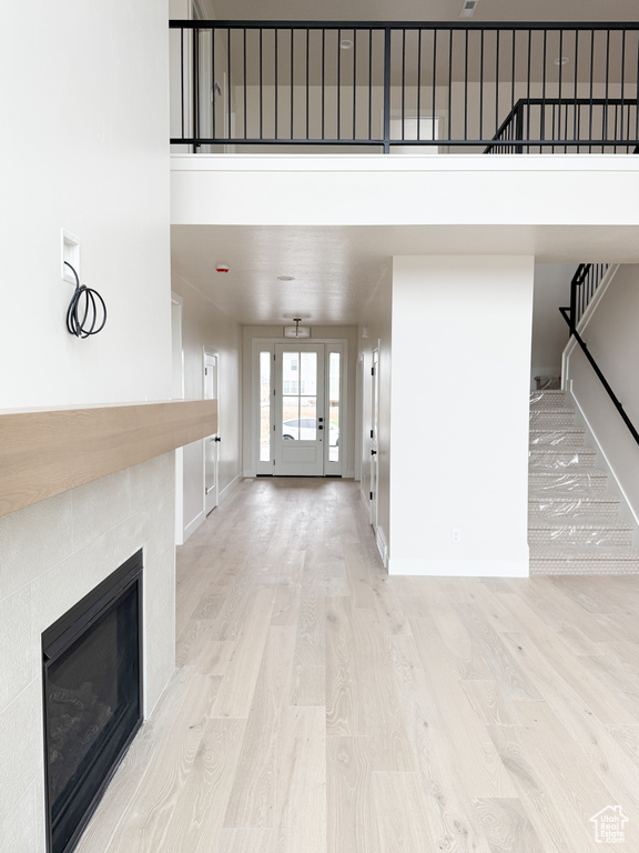 Unfurnished living room featuring a towering ceiling, wood finished floors, baseboards, a tiled fireplace, and stairs