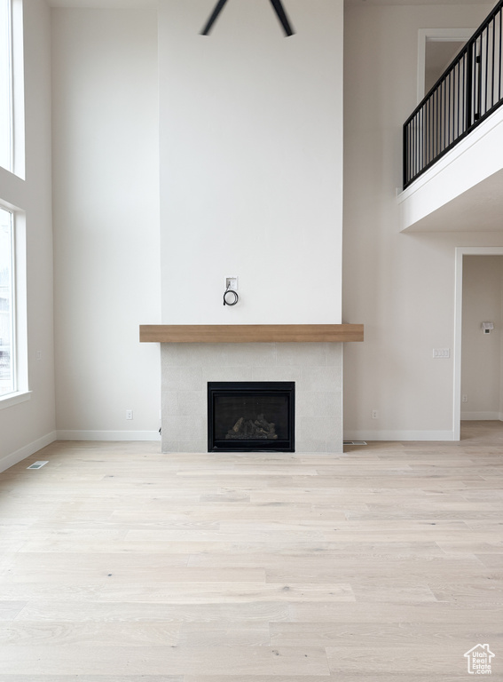 Unfurnished living room with a tile fireplace, wood finished floors, and a towering ceiling