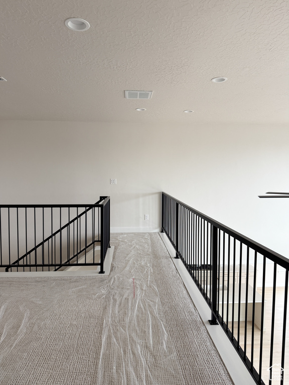 Hall featuring an upstairs landing, a textured ceiling, baseboards, carpet flooring, and visible vents