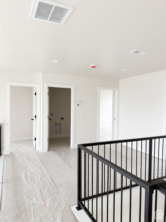 Hallway featuring a textured ceiling, baseboards, visible vents, an upstairs landing, and light colored carpet