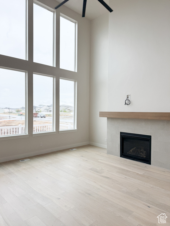 Unfurnished living room featuring a tiled fireplace, visible vents, baseboards, a ceiling fan, and wood finished floors
