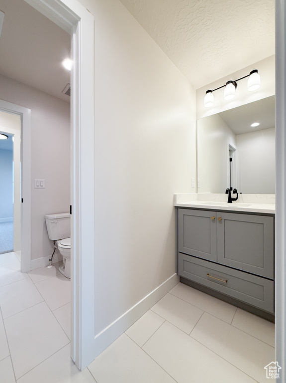Bathroom featuring tile patterned flooring, toilet, vanity, baseboards, and a textured ceiling