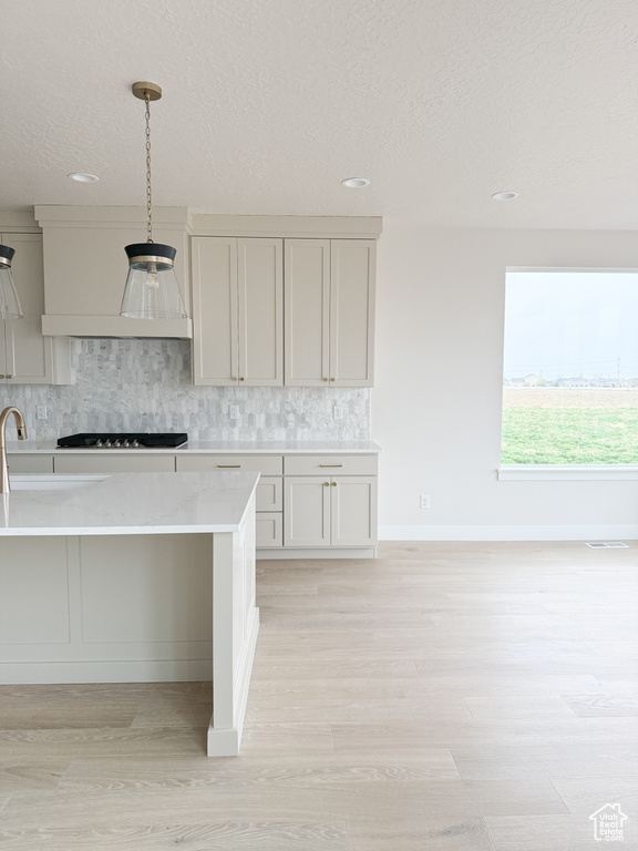 Kitchen with decorative backsplash, light wood-style floors, premium range hood, pendant lighting, and black stovetop